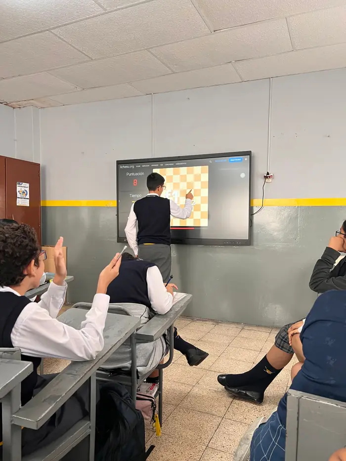 Estudiante del colegio Juan XXIII resolviendo un ejercicio de ajedrez en la pizarra digital mientras sus compañeros levantan la mano