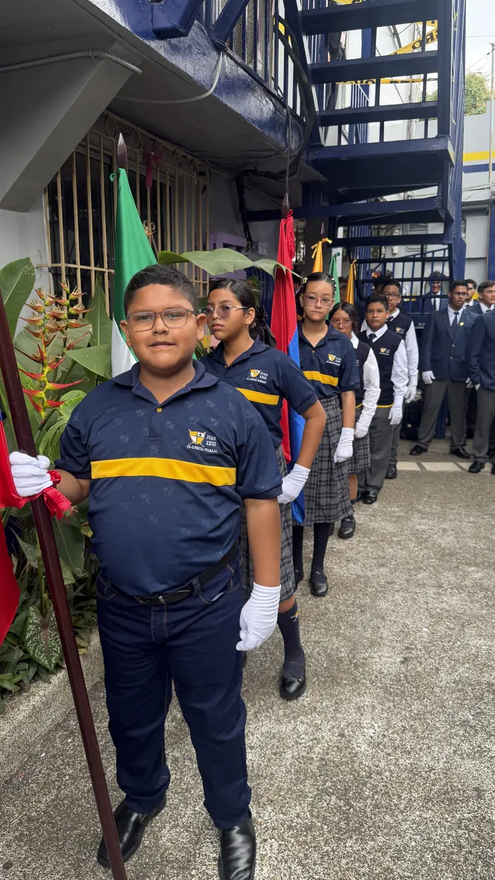 Estudiante del colegio Juan XXIII con guantes blancos sosteniendo una bandera en el Día de la Bandera